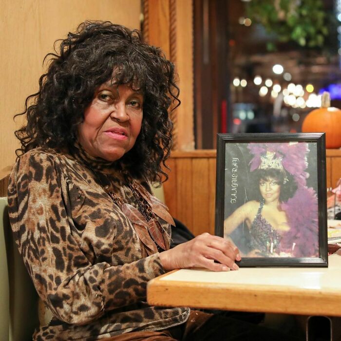 Elderly woman with curly hair holds framed photo in a cozy setting, reflecting moving stories from Humans of New York.