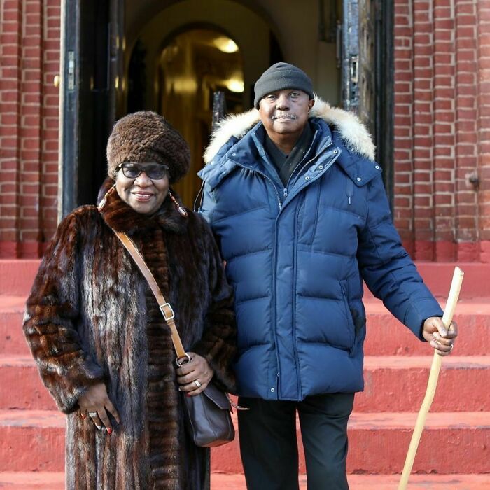 Older couple standing on red steps outside a brick building, showcasing moving stories from Humans of New York.