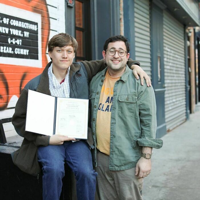 Two men smiling on a New York City street, one holding a certificate, capturing moving stories from Humans of New York.