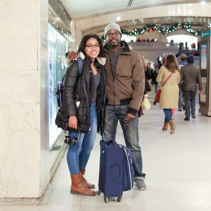 A smiling couple standing with luggage in a busy train station, captured in Humans of New York moving stories.