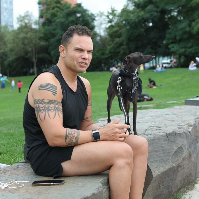 Man with tattoos in black tank top sitting on a rock with a small black dog, a moving story from Humans of New York.
