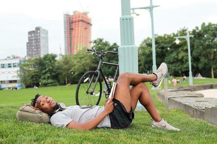 Young man lying on grass in park with book and bike nearby, representing moving stories from Humans of New York.