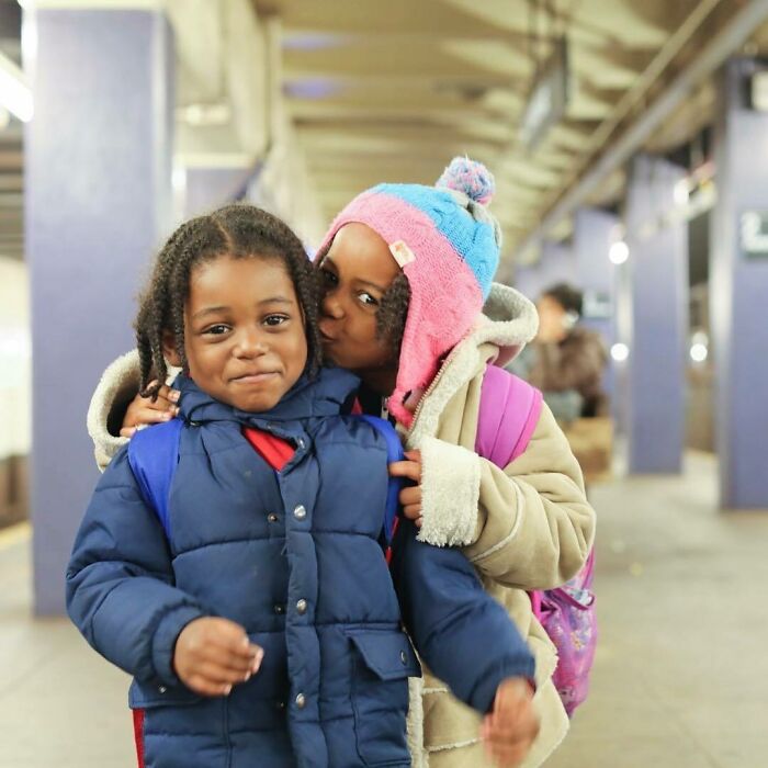 Two children in winter coats sharing a warm moment, capturing moving stories of Humans of New York in an urban setting.