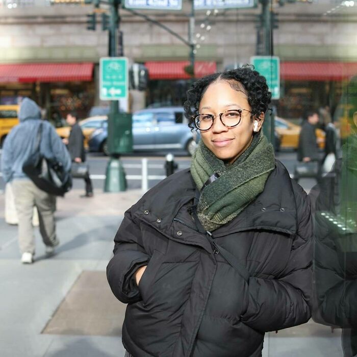 Young woman in glasses and green scarf standing on a busy city street, a moving story from Humans of New York.