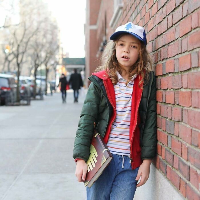 Young person leaning against brick wall on a city street, holding a book, representing humans of New York stories.