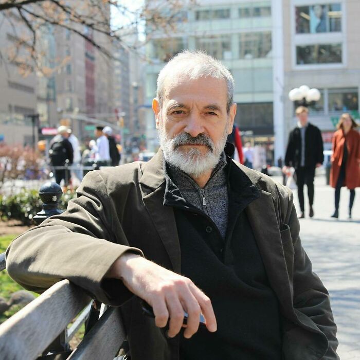 Older man with gray beard sitting on a bench in a city park, captured for moving stories from Humans of New York.