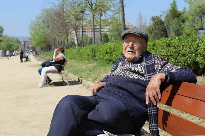 Elderly man sitting on a bench in a park, smiling and enjoying a peaceful moment, reflecting moving stories humans of New York