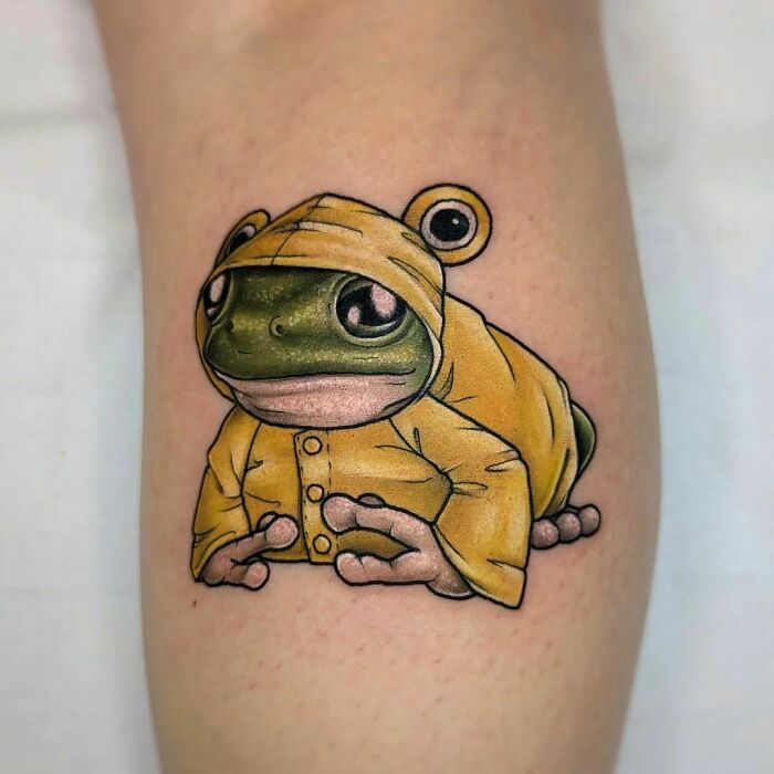 Adorable frog tattoo in a yellow raincoat on a forearm.