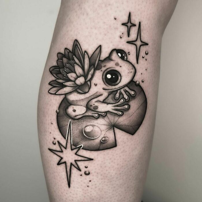 Adorable frog tattoo with lily pad and star designs on the leg.