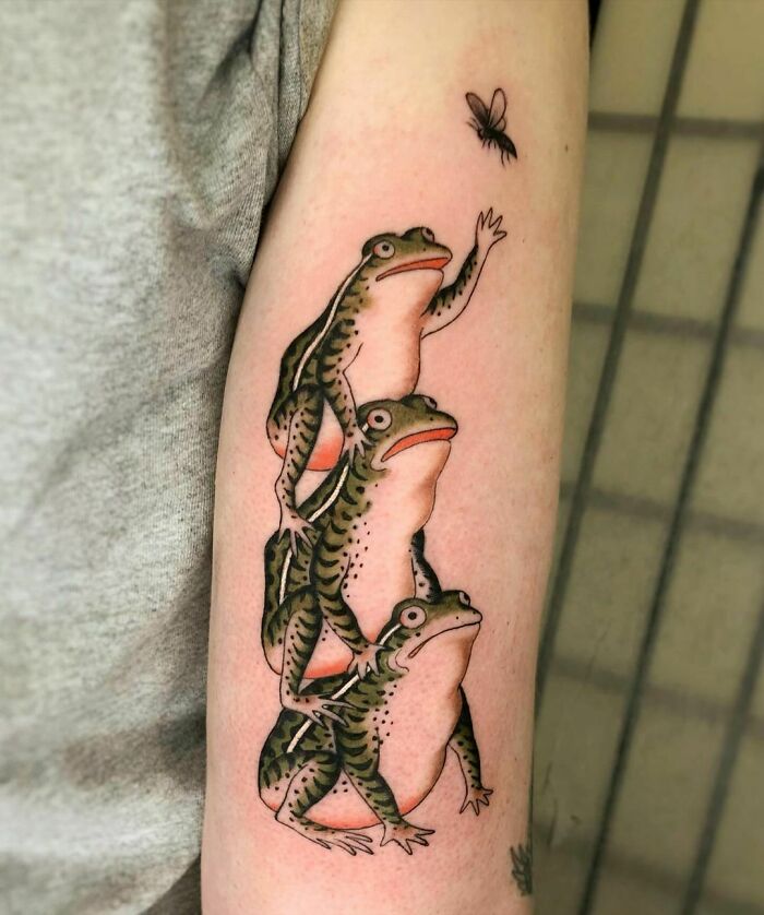Tattoo of three stacked frogs reaching for a fly, showcasing creative frog tattoo art.