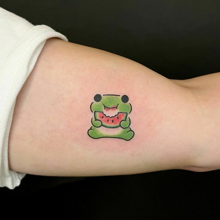Adorable frog tattoo on arm, featuring a cute frog holding a slice of watermelon.