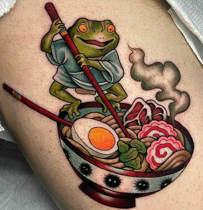A creative frog tattoo featuring a frog in a kimono stirring a steaming bowl of ramen on skin.