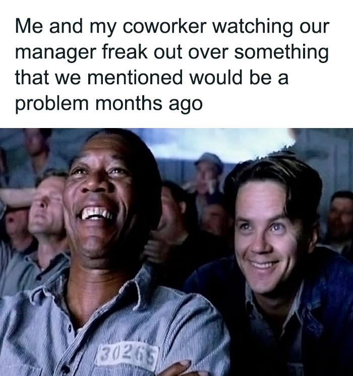 Two coworkers laughing while watching their manager freak out over a problem in a funny work meme.