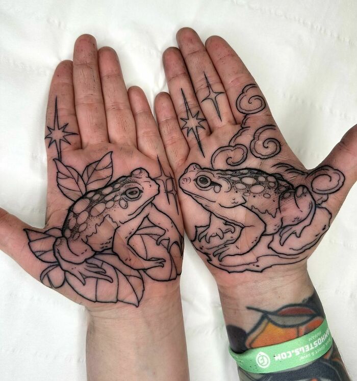 Frog tattoos on both palms featuring intricate designs with leaves and stars.