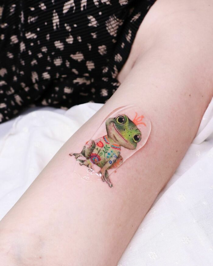 Colorful frog tattoo on a person's arm, showcasing creative and adorable design.