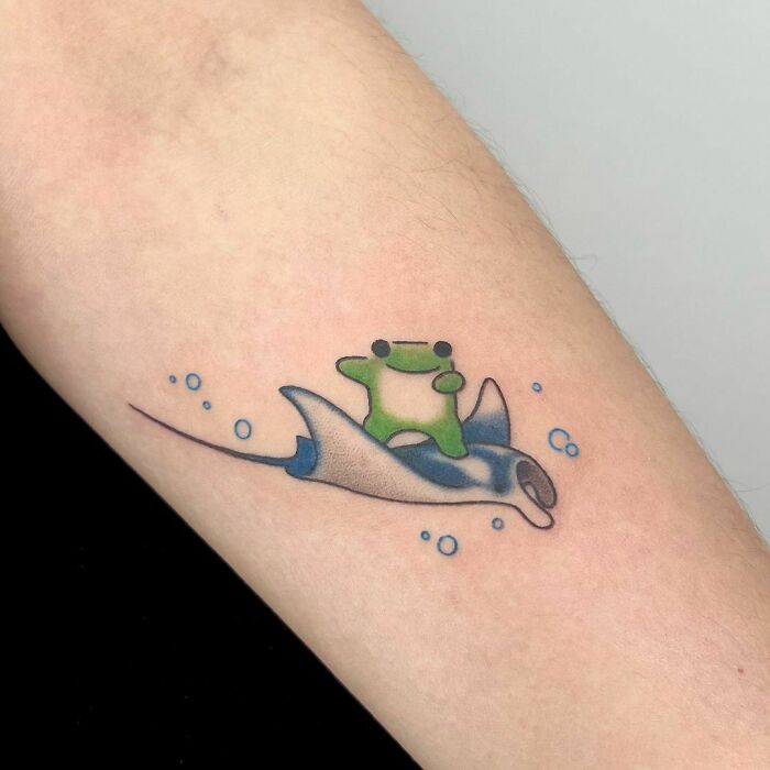 Adorable frog tattoo of a green frog riding a blue stingray with bubbles, showcasing creative and awesome design.