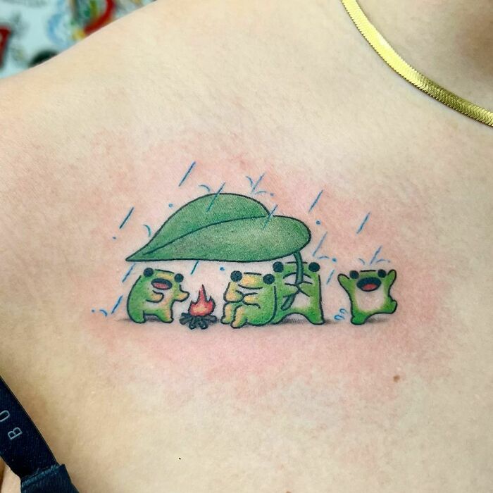 Adorable frog tattoo with frogs under a leaf in the rain, huddled around a campfire.