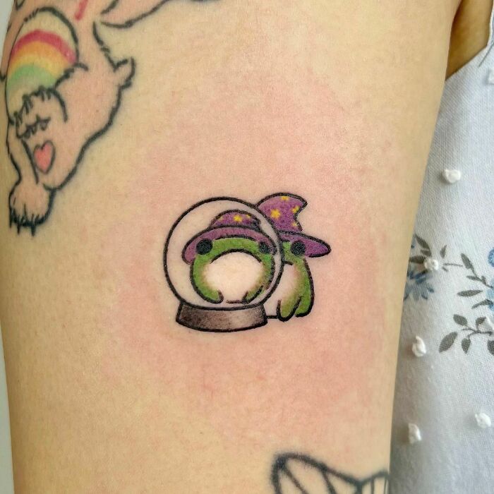 Creative frog tattoo with a witch hat and crystal ball on an arm.