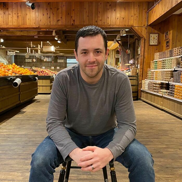 Man sitting on a chair in a wooden market, smiling warmly, representing moving stories from Humans of New York.