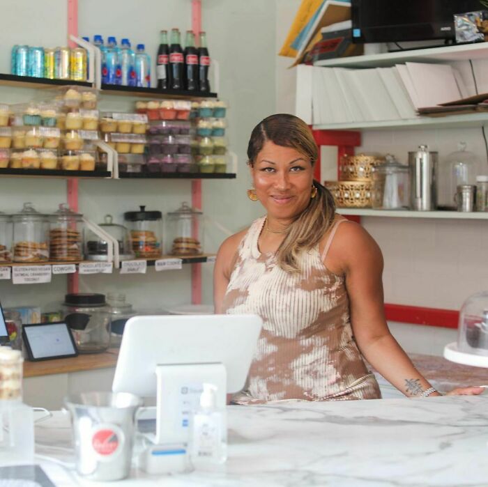 Woman smiling behind a bakery counter with pastries and drinks, a moving story from Humans of New York featured.