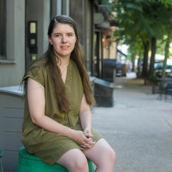 Young woman in an olive dress sitting on a green stool on a city sidewalk, part of moving stories from Humans of New York.