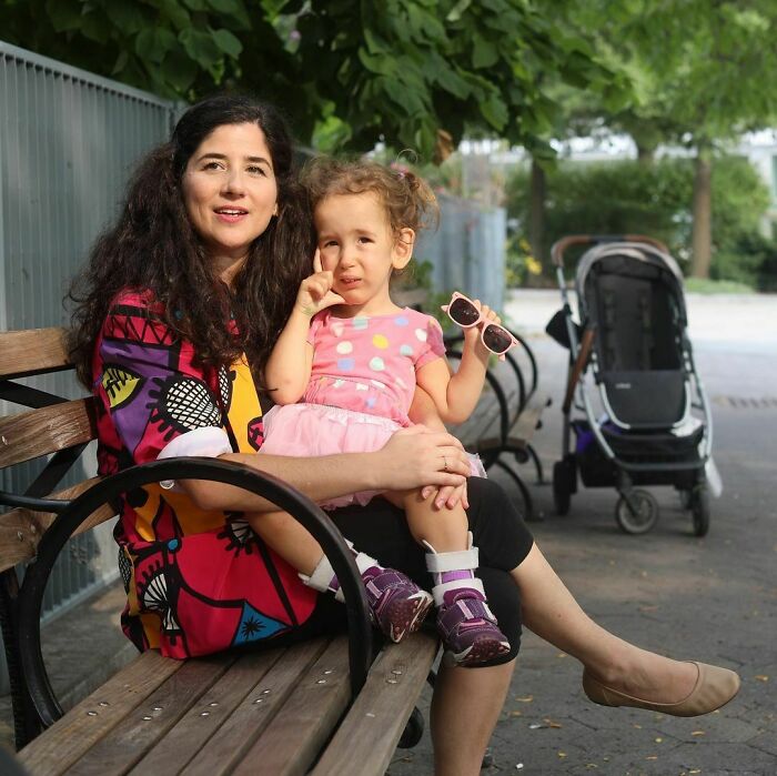 Woman and young girl sitting on a bench in a park, sharing a moment from moving stories of Humans Of New York.