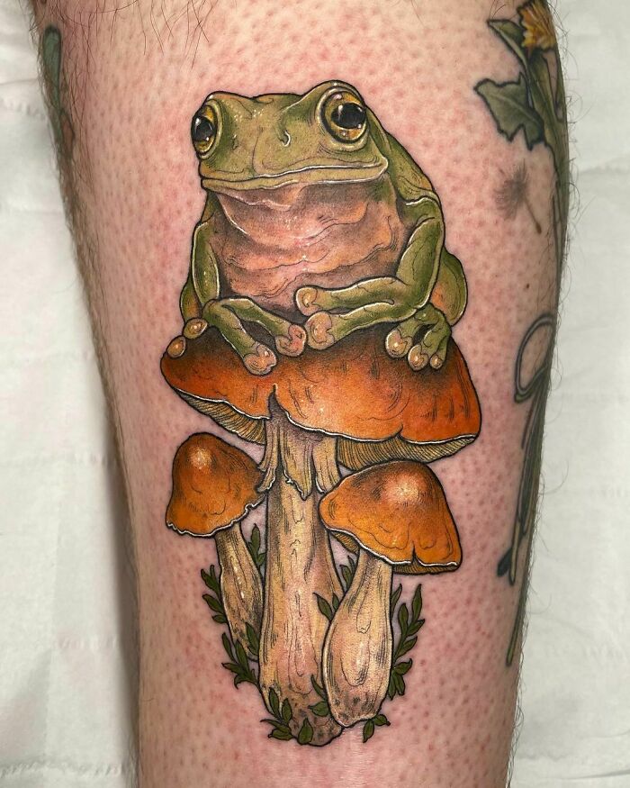 Frog tattoo sitting on orange mushrooms, showcasing creative and adorable design.