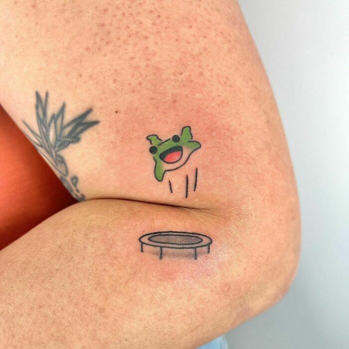Adorable frog tattoo design with a cute frog jumping above a trampoline on a person's arm.