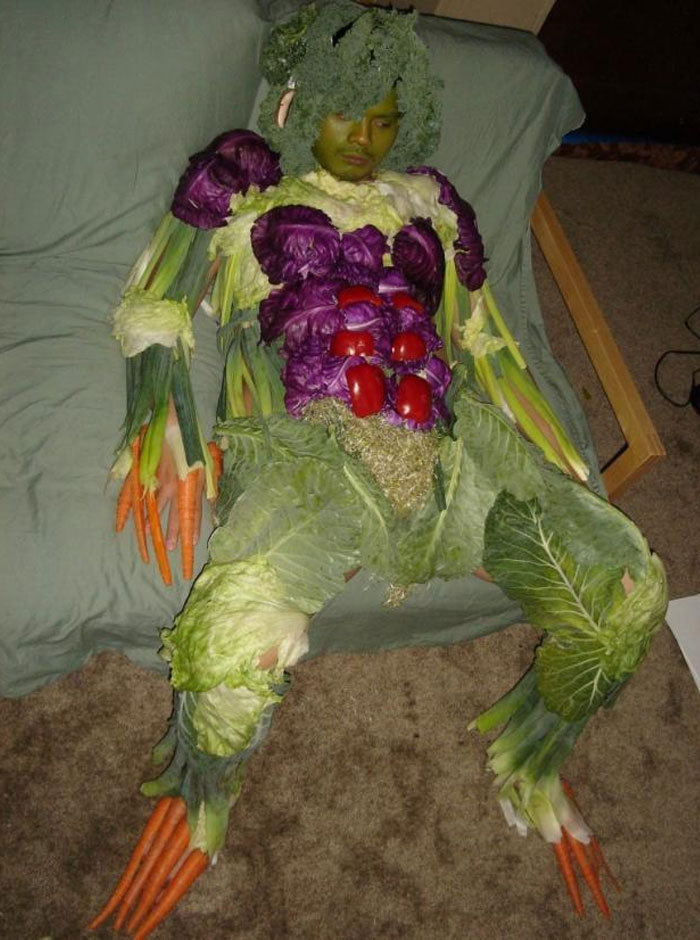 A humorous image of a person dressed entirely in vegetables, resembling a human-vegetable hybrid. Their costume includes carrots for fingers, broccoli for hair, lettuce leaves, cabbage, and red bell peppers covering the body, creating a surreal and quirky appearance. The person appears to be sitting or resting on a couch, adding to the absurdity of the situation. This image could inspire a "funny group chat name" related to vegetables, gardening, or quirky costumes. A humorous image of a person dressed entirely in vegetables, resembling a human-vegetable hybrid. Their costume includes carrots for fingers, broccoli for hair, lettuce leaves, cabbage, and red bell peppers covering the body, creating a surreal and quirky appearance. The person appears to be sitting or resting on a couch, adding to the absurdity of the situation. This image could inspire a "funny group chat name" related to vegetables, gardening, or quirky costumes.