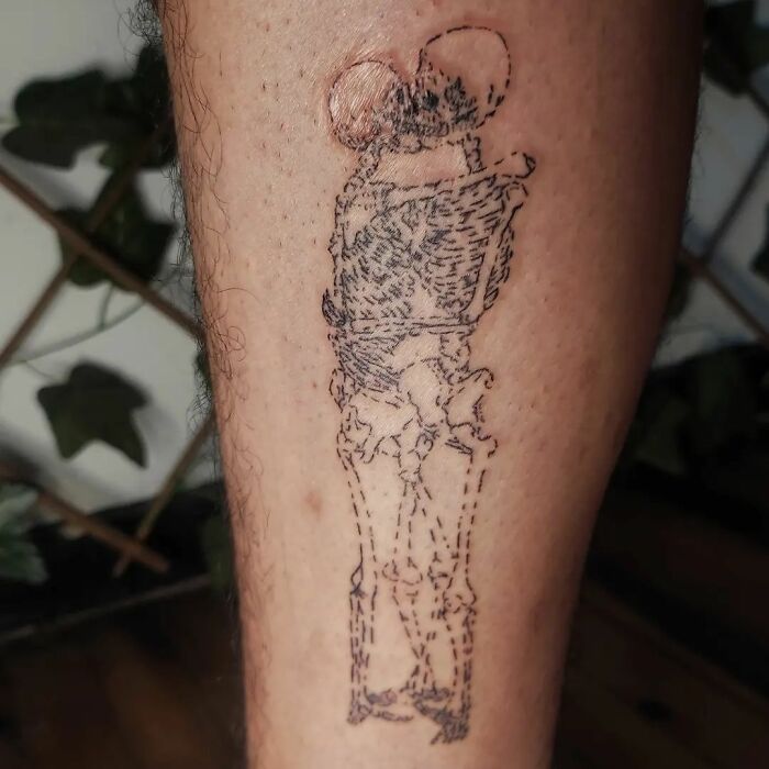 Handpoke tattoo of two skeletons embracing on a person's leg.