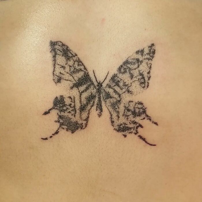 Handpoke tattoo of a detailed butterfly on skin by a tattoo artist.