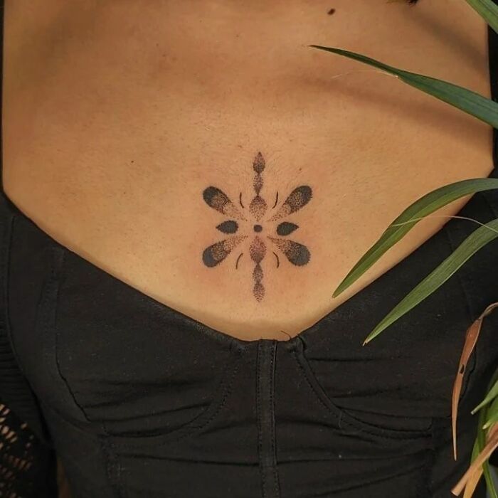 Handpoke tattoo of abstract design on chest, with a black top and green leaves in the foreground.
