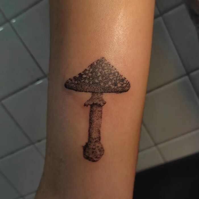 Handpoke tattoo of a mushroom on a forearm, showcasing detailed artistry and unique design.