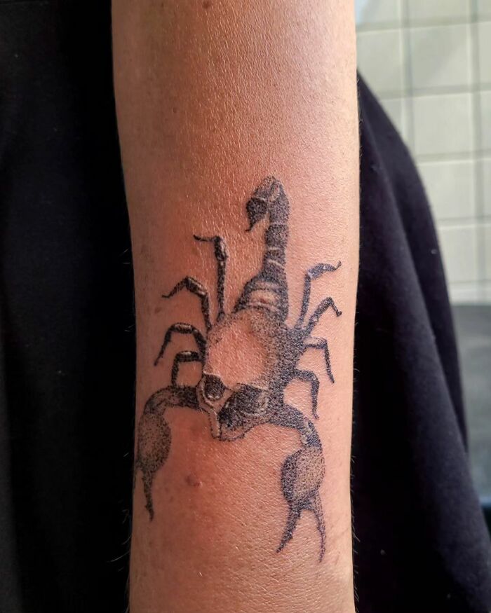 Handpoke tattoo of a scorpion on a forearm, showcasing intricate black ink design.