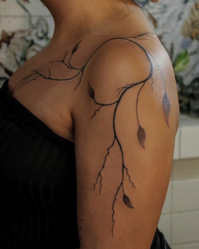 Handpoke tattoo of branches and leaves on an upper arm, showcasing intricate and natural design.