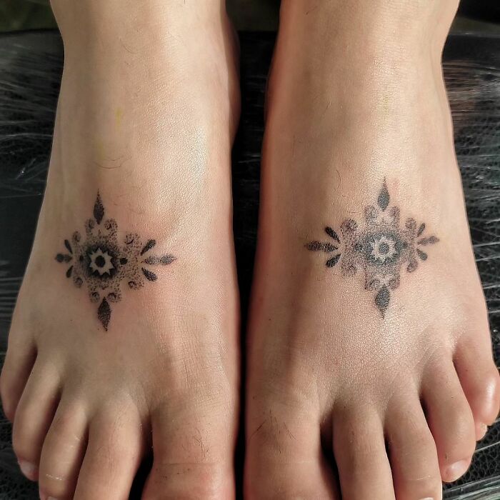 Symmetrical handpoke tattoos on feet, showcasing a detailed floral design created by a tattoo artist.