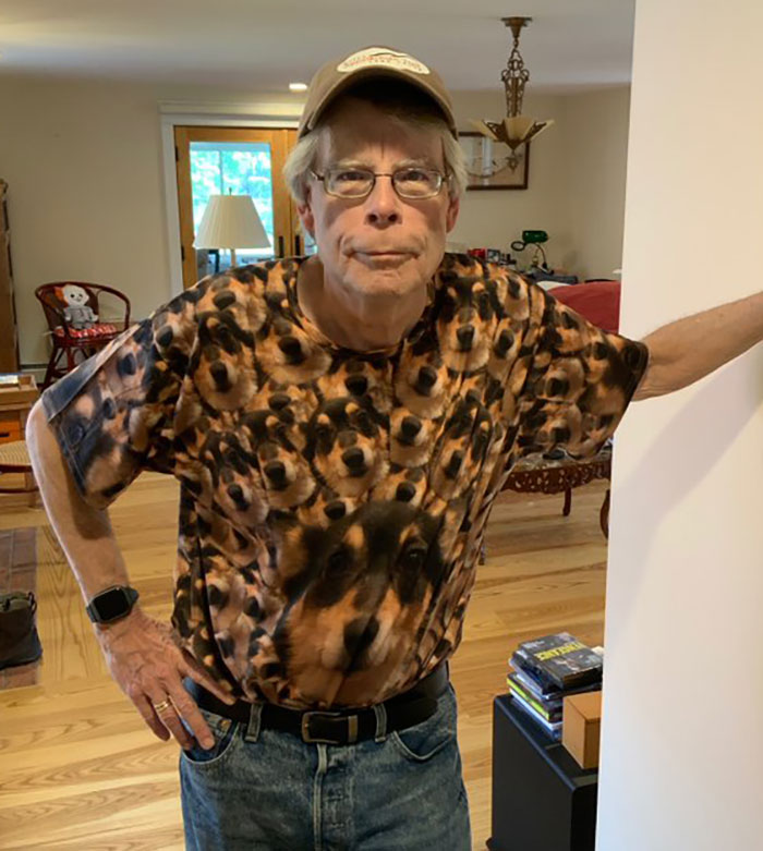 Person in a cap and dog-themed shirt stands indoors, hands on hips, looking directly at the camera.