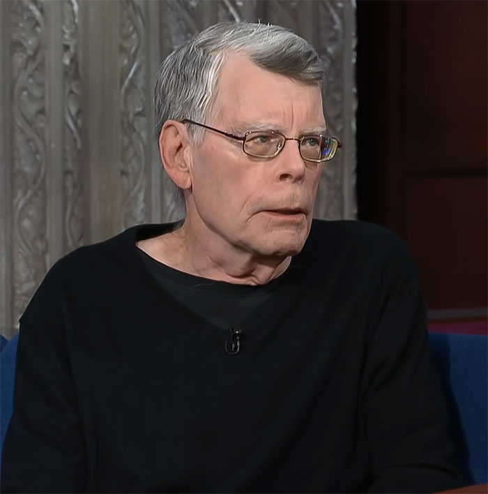 Stephen King sitting during an interview, wearing glasses and a black sweater.