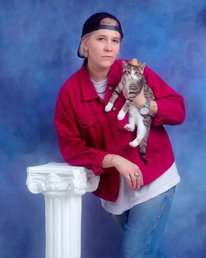 Person wearing a red jacket holding a cat with a tiny hat, posing for quirky portraits of pets and their owners.