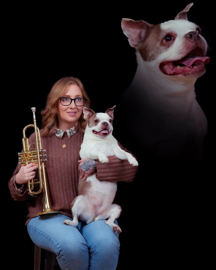 Woman holding a trumpet and her dog in a quirky pet and owner portrait against a black background.