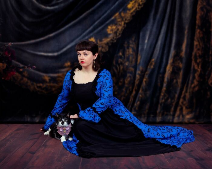 Woman in a blue and black dress posing with her black and white cat in a quirky pet and owner portrait session.