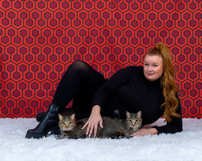 Photographer captures quirky pet and owner portraits featuring a woman in black with two tabby cats on a white rug.