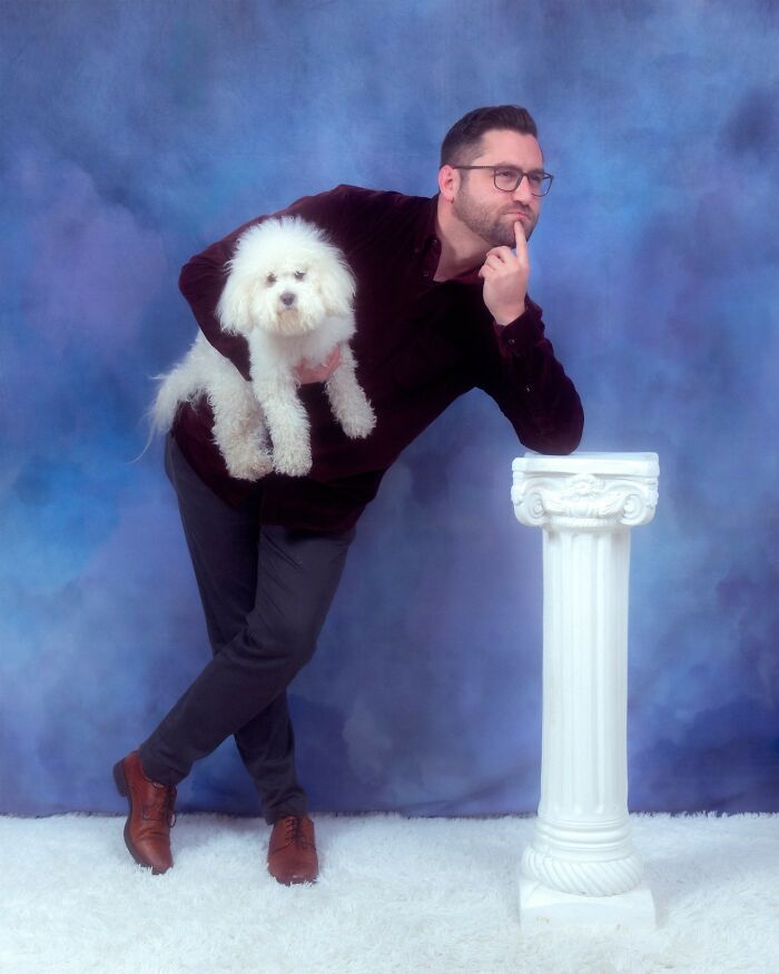 Man holding fluffy white dog, posing thoughtfully next to white column in a quirky pet and owner portrait session.