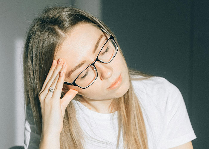 Young woman with glasses touching her forehead, appearing stressed, illustrating adult problems people face in life.
