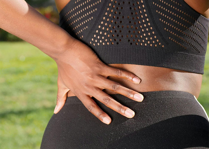 Close-up of a person holding their lower back outdoors, illustrating adult problems related to physical pain and health.