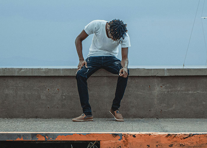 Young man sitting alone on a concrete ledge looking down, representing adult problems people wish someone warned them about.