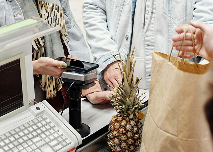 Customer using mobile phone for contactless payment at checkout, illustrating common adult problems in daily life.
