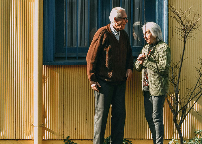 Elderly couple standing outside a yellow building, representing adult problems people wish they were warned about earlier.