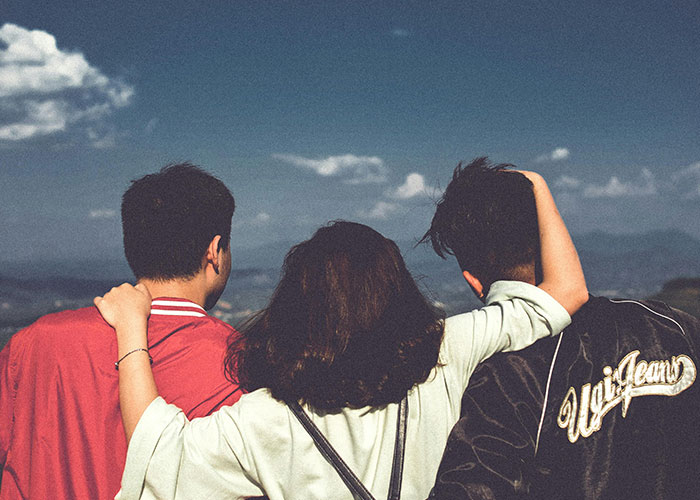 Three friends embracing outdoors under a blue sky, reflecting on adult problems people wish they knew earlier in life.