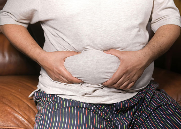 Person wearing a beige shirt and striped pants holding their stomach, illustrating common adult problems and challenges.